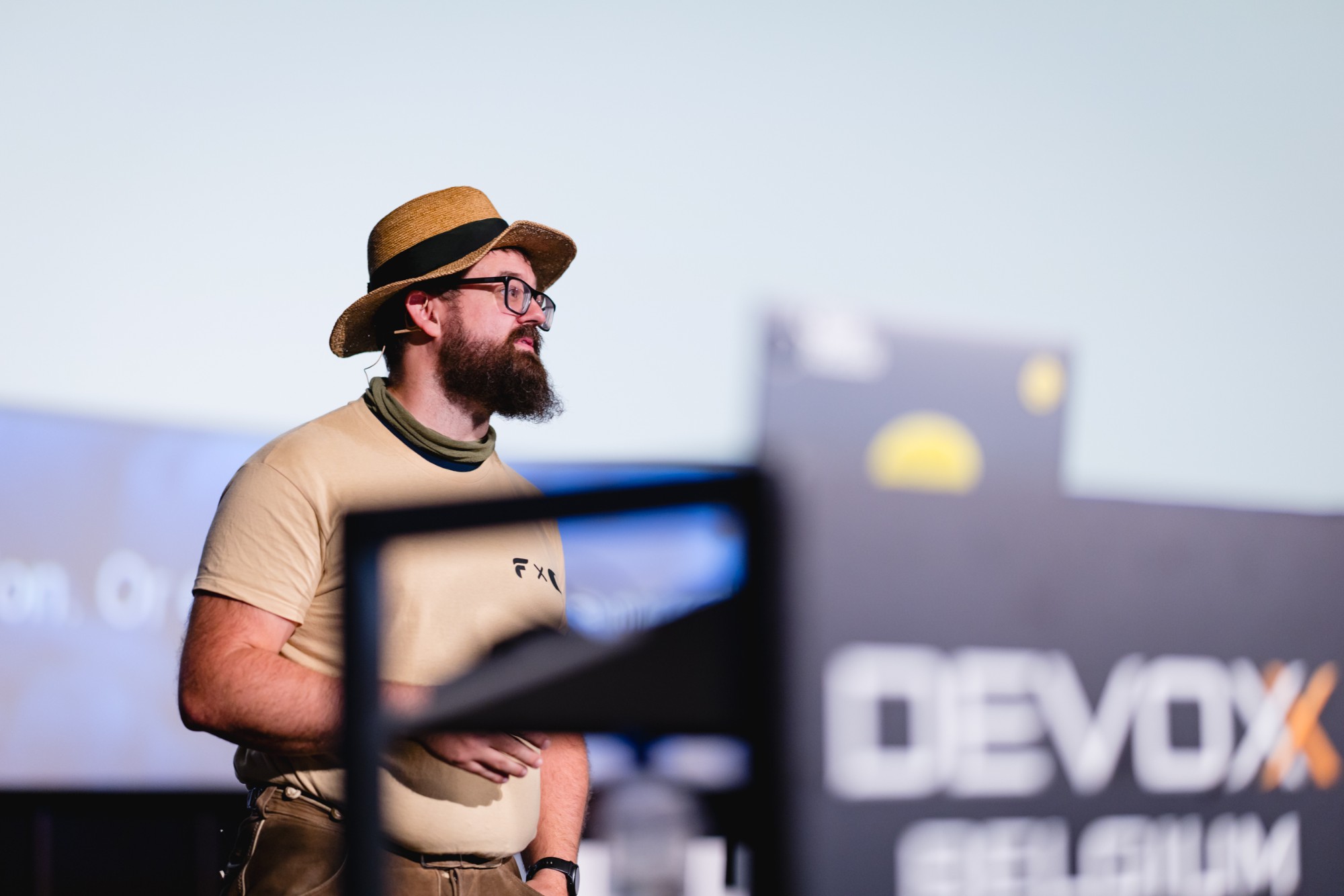 Simon in a straw hat on stage at Devoxx Belgium, the conference logo blurred in the foreground